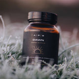 Supplement bottle labeled 'Dawn' on grass with frost.