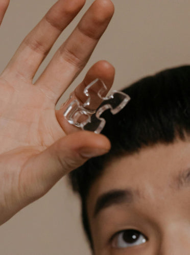 Person holding a clear puzzle piece near their hair against a neutral background